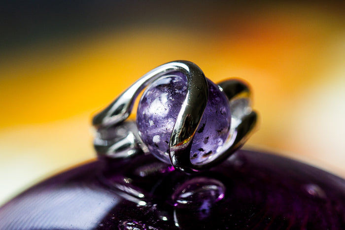 Close-up of a sterling silver ring featuring a purple 12mm glass marble infused with cremation ash.