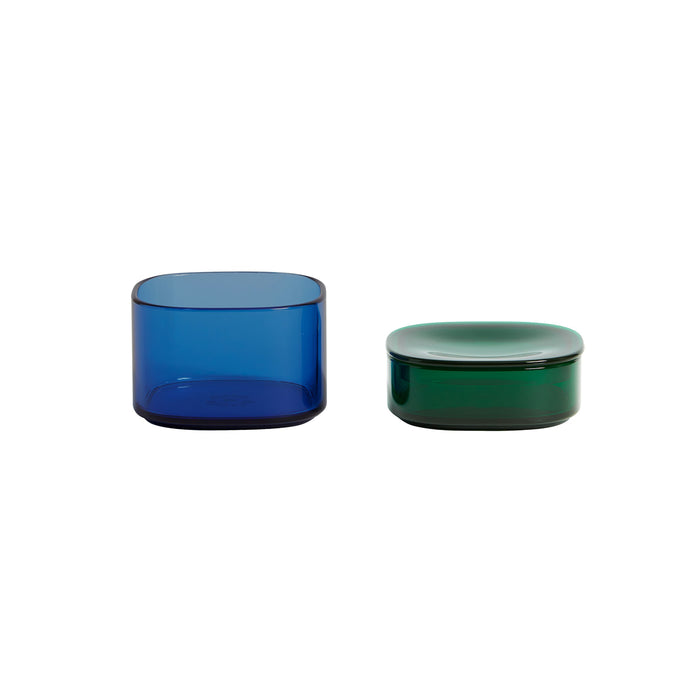 Two Storage Gems by Open Spaces are displayed on a white backdrop. The tall, open-topped one is blue, and the shorter green container comes with a matching lid. Both showcase a sleek, minimalist design made from crystalline acrylic.