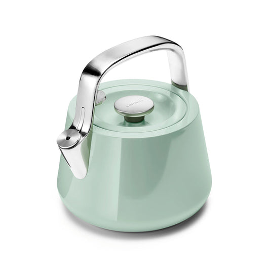 A mint green Stovetop Whistling Tea Kettle by Caraway, made from non-toxic stainless steel with a shiny silver handle and lid. It has a modern design with a wide, sturdy base.