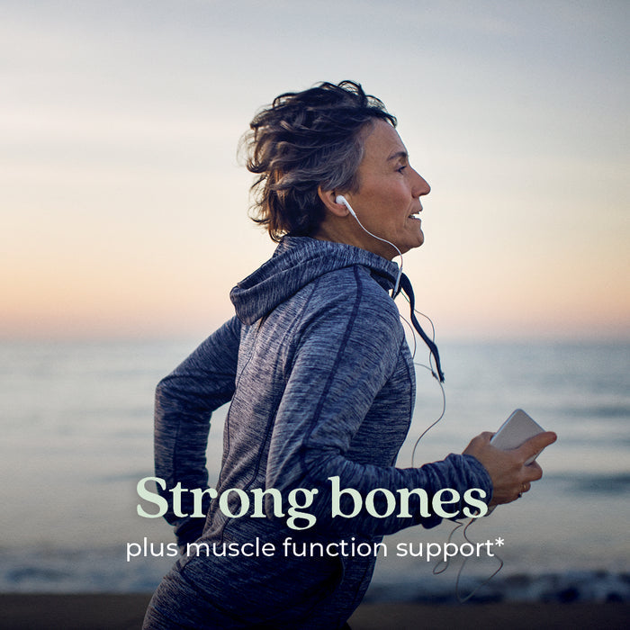 A person in athletic clothing jogs by the ocean at sunset, smiling and listening to music with earbuds. Text: Support strong bones and muscle function* with New Chapter Strength Support Vitamin D3+ Gummies, Mixed Berry Flavored.
