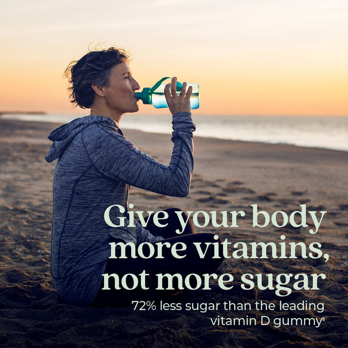A person in athletic wear sips from a water bottle on a beach at sunset. Text: Power up with New Chapter Strength Support Vitamin D3+ Gummies, Mixed Berry Flavored—72% less sugar than leading vitamin D gummies.