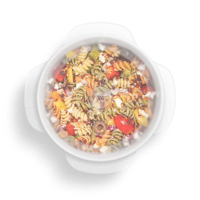 A W&P Stretch Lid covers a round bowl containing rotini pasta salad with cherry tomatoes, olives, red onions, and feta cheese, providing an ideal food storage solution.