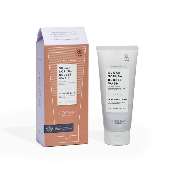 A tube and box of VOESH New Yorks Sugar Scrub + Bubble Wash for Scalp and Body in Lavender Land scent, enriched with vegan probiotics. The white and lavender packaging showcases its vegan benefits amidst creative design elements.