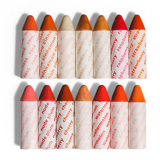The Super Fan Pack by Axiology showcases twelve multi-use lipstick crayons in two rows on a white background. Each vegan, plastic-free crayon is wrapped in white paper, flaunting unique colors and names like rosewood, raspberry, nude plum, and watermelon. Perfect for eco-conscious beauty lovers.