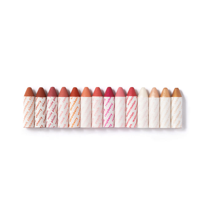 The Super Fan Pack by Axiology features 13 crayon-shaped, plastic-free vegan lipsticks in shades ranging from nude to bright red, each with a white wrapper and pink diagonal text, neatly displayed on a pristine white background.