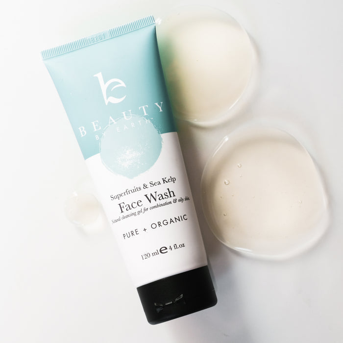 A Beauty by Earth Superfruits & Sea Kelp Facial Cleanser tube for oily skin sits on a white surface. Its light blue and white design highlights its superfruit and sea kelp formula, while two liquid droplets lie nearby.