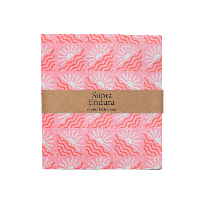 A pink Supra Endura Swedish Dish Cloth with red and white sun pattern, wrapped in a brown band labeled "Swedish Dish Cloths"—eco-friendly, super absorbent, and ideal for daily cleaning.