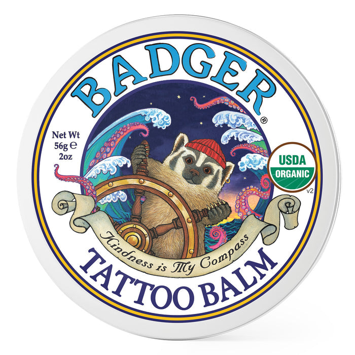 Badger Balms Tattoo Balm features a badger in a red hat navigating waves and stars, with Kindness is My Compass as its motto. Perfect for tattoo aftercare, this 56g/2oz USDA Organic moisturizer ensures your skin feels cared for.