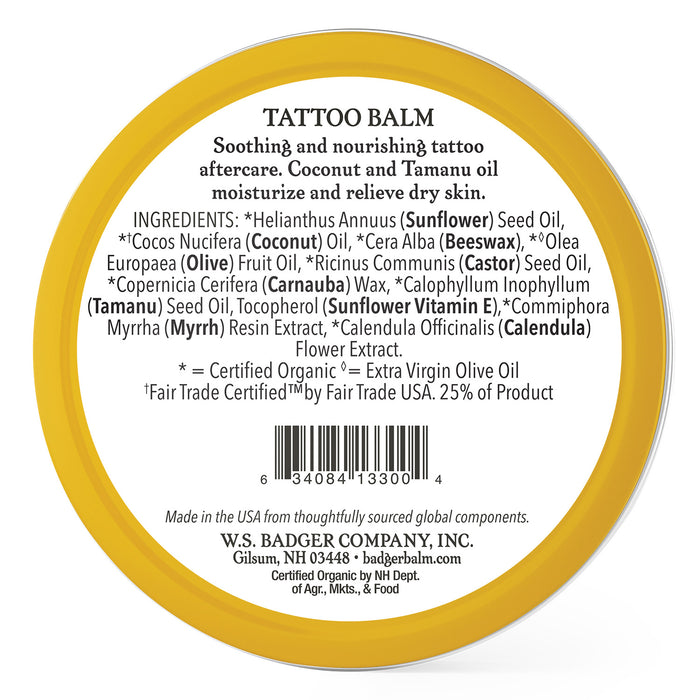 A round tin of Badger Balm Tattoo Balm featuring a yellow edge and white label with ingredients like sunflower seed oil, coconut oil, and Vitamin E. The label emphasizes its soothing, moisturizing, and nourishing properties for tattoos and highlights its organic, fair trade certifications.