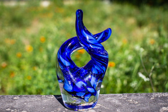 Blue Taurus glass sculpture featuring two crossed horns against a blurred outdoor backdrop