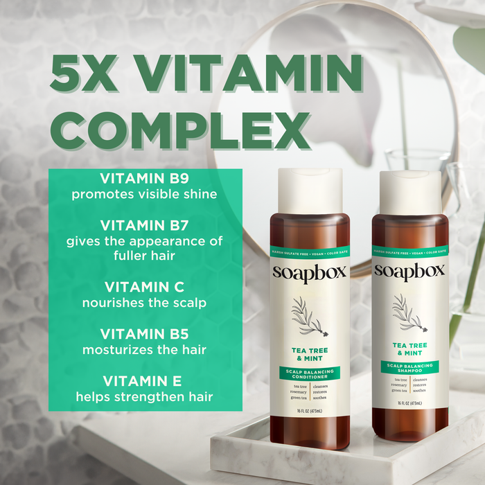 Two bottles of Soapbox Tea Tree & Mint Scalp Balancing Conditioner rest on the bathroom counter, providing lightweight hydration. A text box emphasizes the 5X Vitamin Complex with Vitamins B9, B7, C, B5, and E benefits for hair care. A mirror and plant enhance the background decor.
