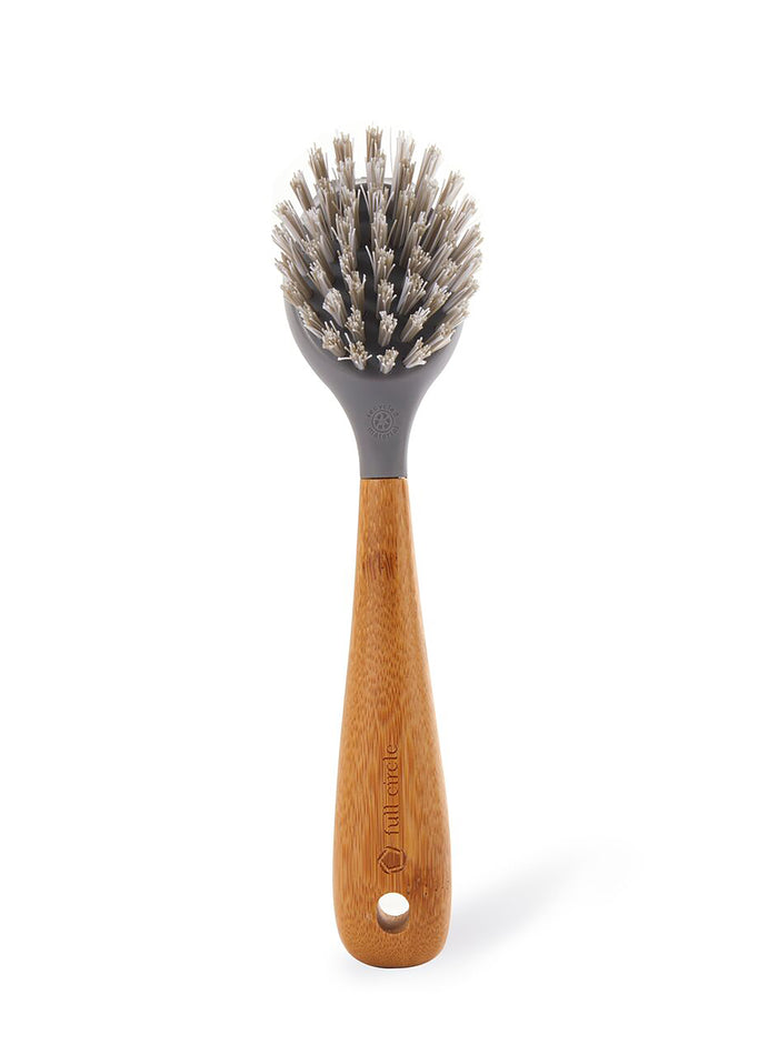The Tenacious C Cast Iron Brush by Full Circle features a round, gray bristle head made from recycled nylon. It has a sleek bamboo handle with a hanging hole and densely packed bristles for effective cleaning.