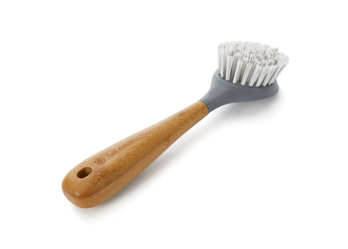 The Tenacious C Cast Iron Brush by Full Circle features an eco-friendly bamboo handle engraved with full circle and a gray plastic head with recycled-nylon white bristles. Ideal for cast iron care, it has a hanging hole and is perfect against clean white backgrounds.