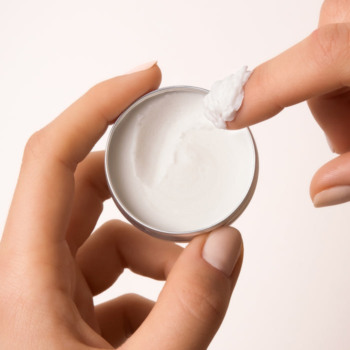 A hand holds an open tin of The Body Wash Concentrate Travel Mini by Everist, while another scoops out the product against a neutral light background.