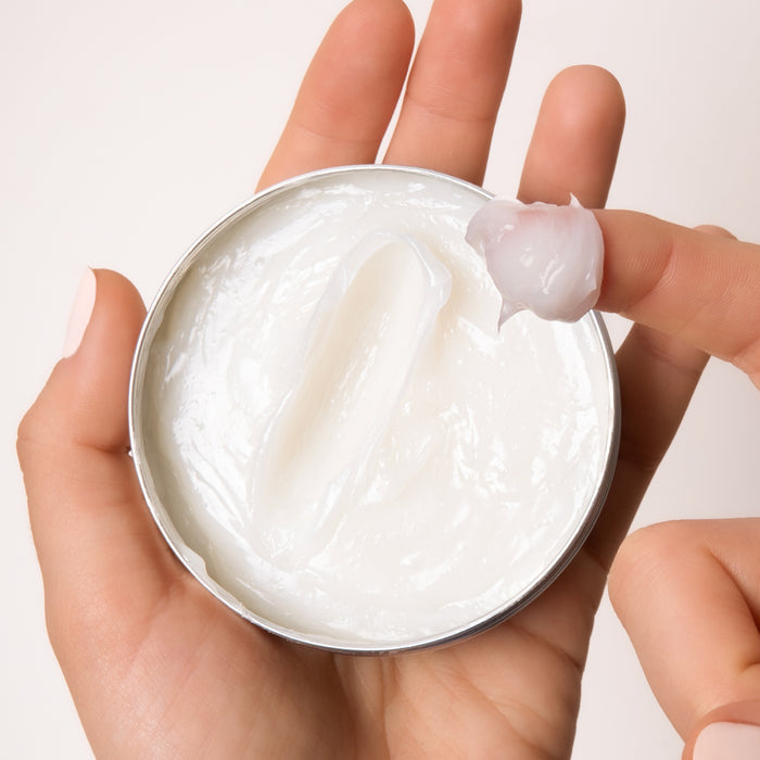 A hand holds an open round tin of Everists The Deep Conditioning Concentrate, while another scoops out the hydrating formula—suitable for all hair and skin types and enriched with natural rosemary oil.