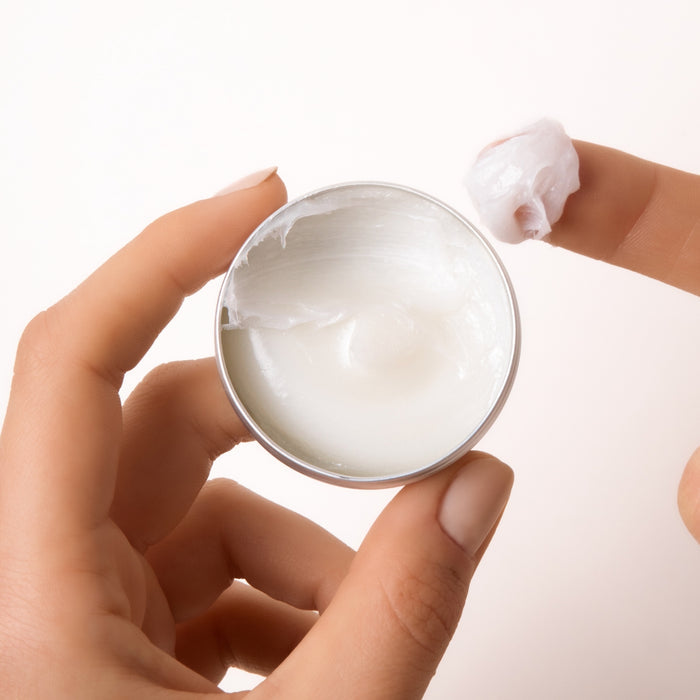 A hand holds Everists The Deep Conditioning Concentrate Travel Mini, scooping out the rich cream—a blend of haircare and skincare—against a light background.