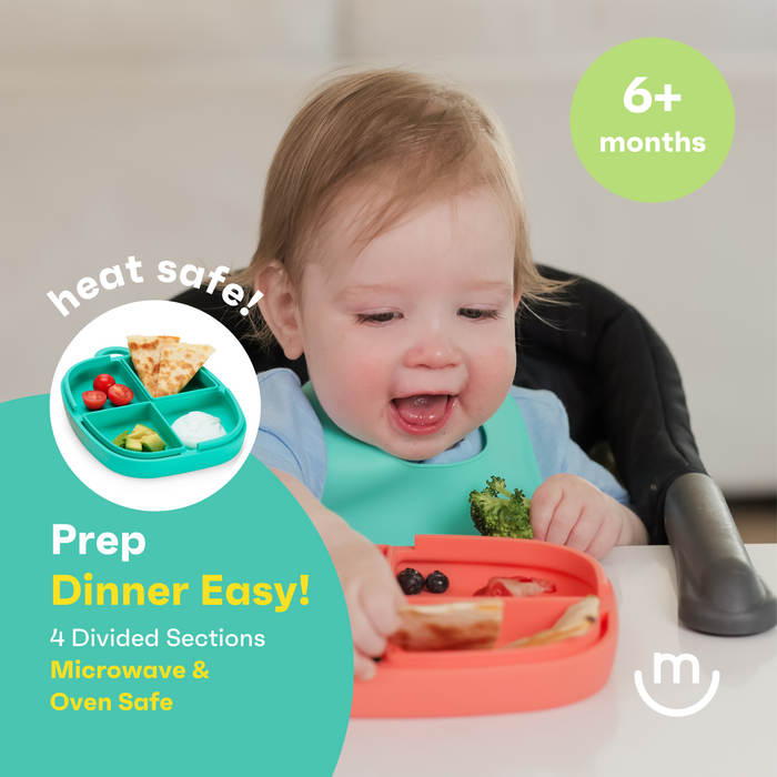A baby enjoying a meal in a high chair. They are wearing a blue bib and holding an orange divided plate with fruit and a slice of bread. Text on the image highlights the plate’s features, including being heat safe and suitable for 6+ months.