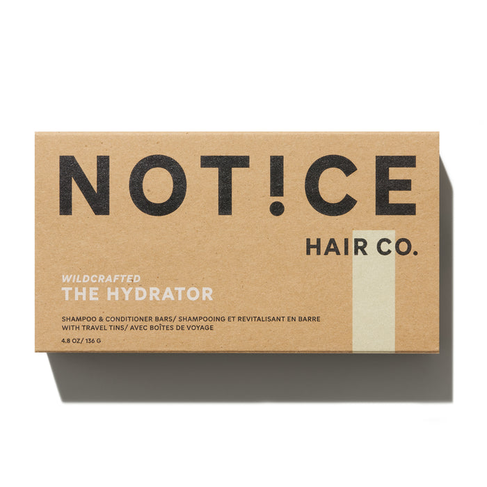 A brown box displays NOT!CE Hair Co in black and The Hydrator in white, containing hydrator shampoo and conditioner bars for plastic-free hair care; travel tins included. Shadow is cast to the right.