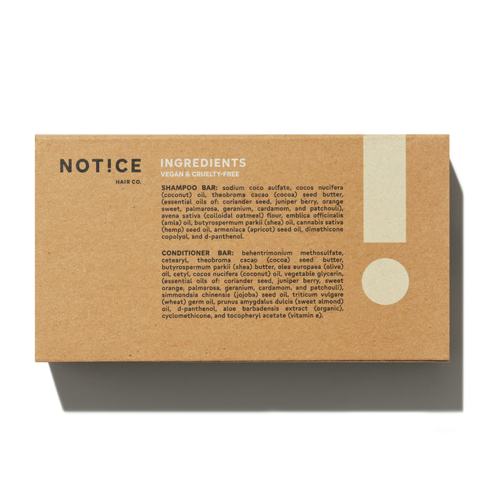 The Hydrator Travel Set from NOT!CE Hair Co comes in a brown rectangular box listing ingredients for its vegan, cruelty-free shampoo and conditioner bars. The box, featuring black and white text and a large exclamation mark, promotes plastic-free hair care.