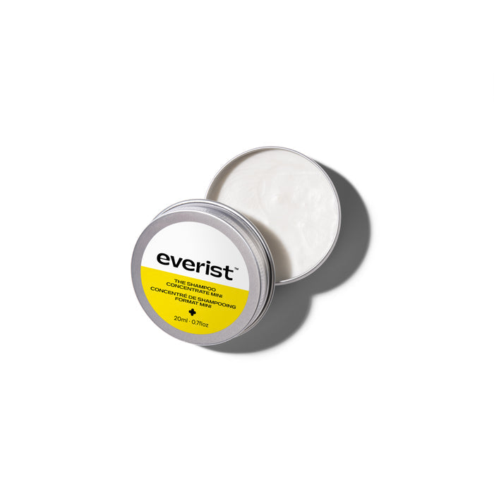 A round, silver tin container of Everist’s The Shampoo Concentrate Travel Mini sits open on a white background, revealing a creamy, plant-based formula. The lid features the Everist label in yellow and white with product information.