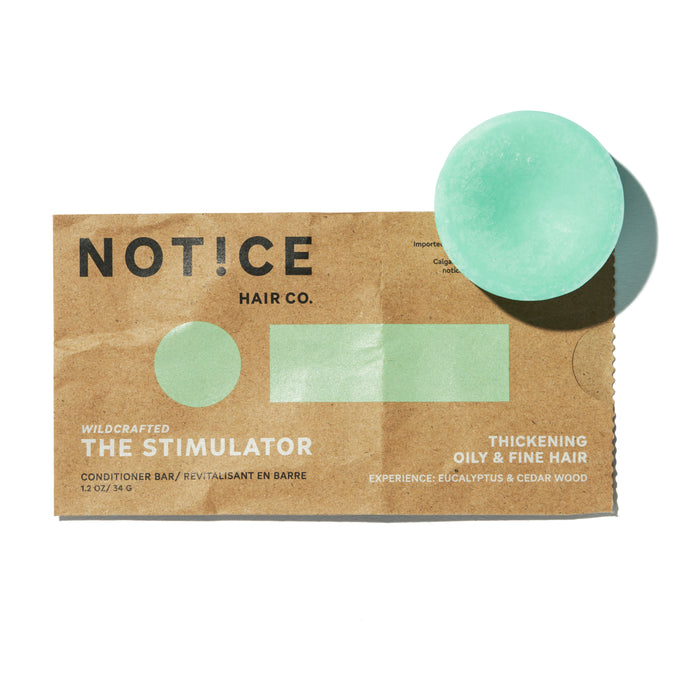 A circular green The Stimulator conditioner bar by NOT!CE Hair Co. rests on brown packaging, promoting hair growth and thickening for oily and fine hair with invigorating eucalyptus and cedar wood scents in a plastic-free solution.
