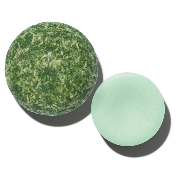 The Stimulator Travel Set by NOT!CE Hair Co features a round, textured shampoo bar with French green clay and a smooth, light green conditioner bar. On a white background, the shampoos mottled design contrasts beautifully with the solid-colored conditioner, both showcasing our brands quality.