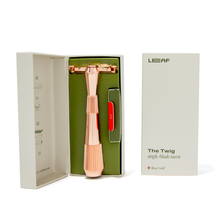 A rose gold, metal safety razor with a single-edge blade and textured ergonomic handle is shown partly in its open box. The box displays the Leaf Shave branding and reads The Twig Plastic-Free Razor.