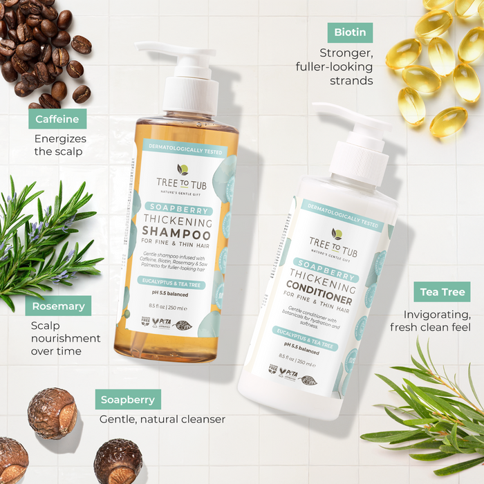 Tree To Tub Volumizing Caffeine & Biotin Shampoo and Conditioner for Fuller, Thicker Hair are displayed on a light surface surrounded by soapberries, rosemary, tea tree, biotin capsules, and coffee beans.