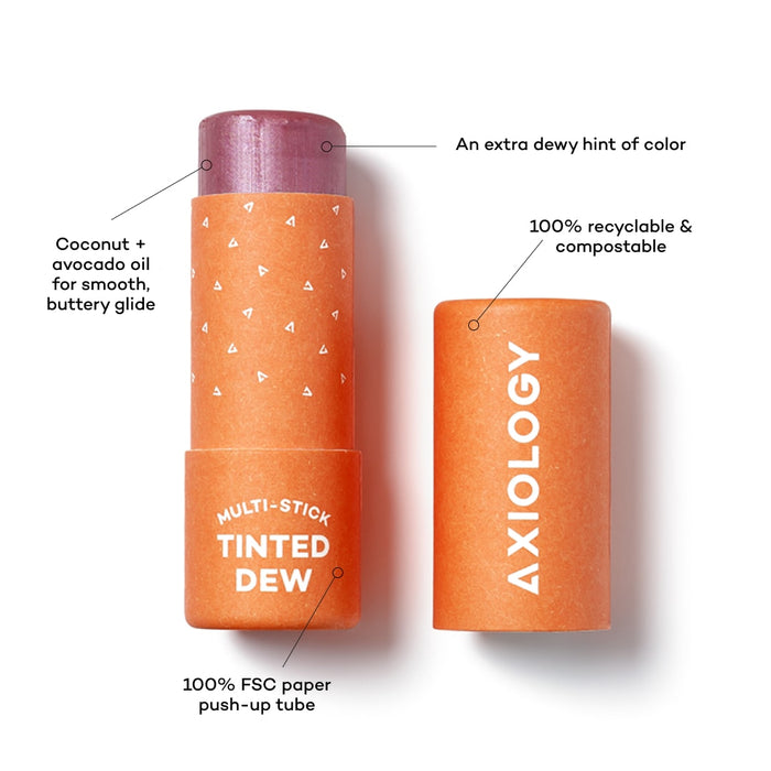 A partially opened Axiology multi-stick labeled "Tinted Dew," displaying a purple hue. The packaging highlights its features: 100% FSC paper push-up tube, 100% recyclable &amp; compostable, contains coconut &amp; avocado oil for smooth glide, and offers an extra dewy hint of color.