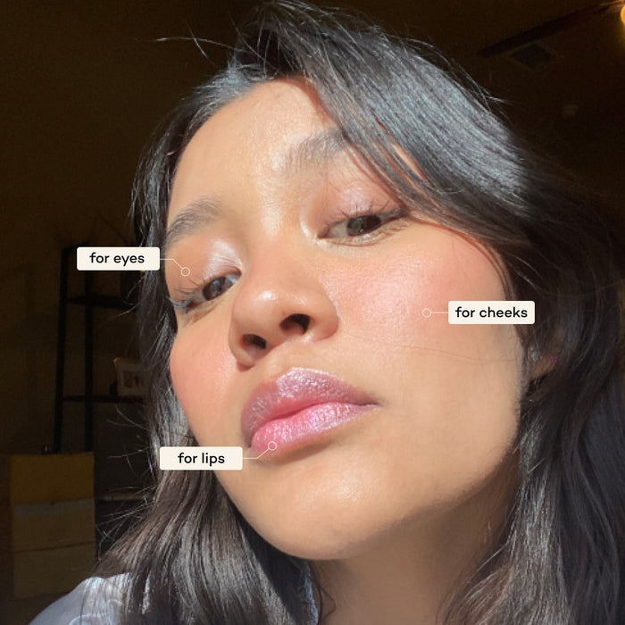 Close-up of a person with long, dark hair and radiant, glowing skin. The face has been labeled to indicate different cosmetics or skincare use: "for eyes," "for cheeks," and "for lips." The person is looking towards the camera with a serene expression.