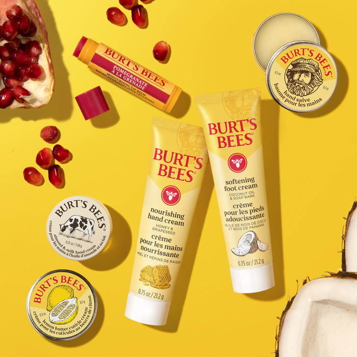 Burt’s Bees Tips & Toes Set showcases skincare essentials—Hand Cream, Pomegranate Lip Balm, and balm tins—displayed on a bright yellow background with coconut pieces and pomegranate seeds for a vibrant look.