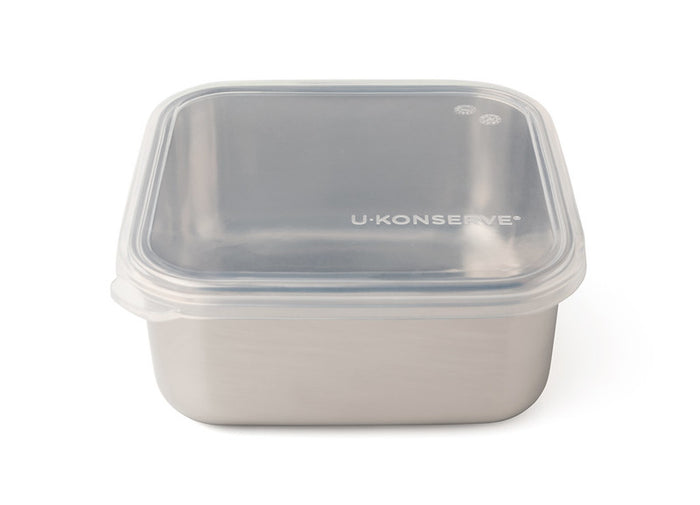 The To-Go Medium Container, a square stainless steel food container by U-Konserve, features a clear plastic lid with a small steam vent. The U-Konserve branding emphasizes their dedication to eco-friendly, plastic-free, sustainable food storage solutions.