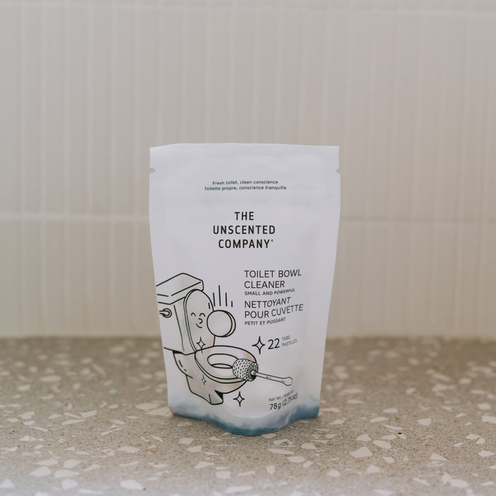 A white pouch of The Unscented Company Toilet Bowl Cleaning Tabs rests on a speckled countertop, featuring minimalist toilet and bubble illustrations and English/French text—ideal for sustainable hygiene.