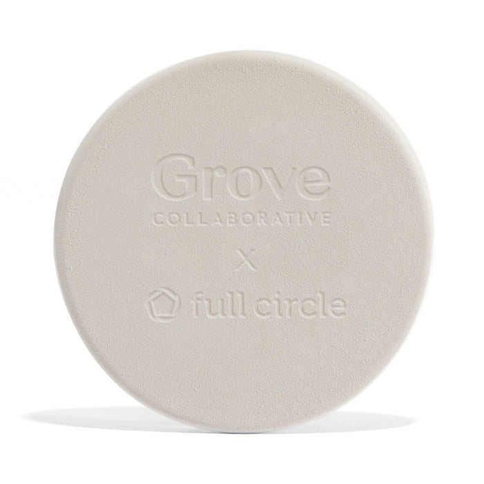 The Grove Co. Toilet Brush Drip Stone Refill is a circular light beige sponge, infused with all-natural diatomaceous earth, boasting Grove Collaborative x Full Circle embossed on its surface. It stands upright against a white background, helping prevent bacteria and mold for optimal cleanliness.