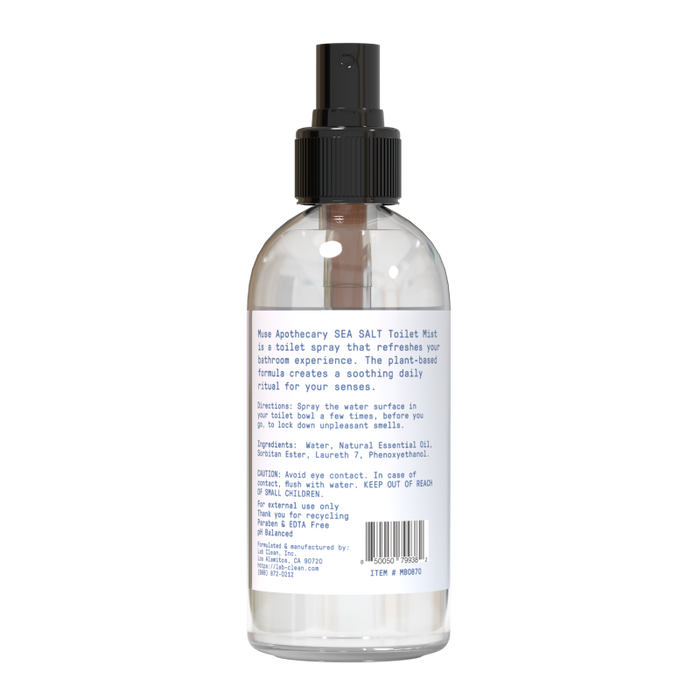 The clear bottle with a black spray nozzle contains Muse Apothecary Toilet Spray. The label includes blue text detailing its plant-based formula, instructions, ingredients, and caution information. Enhance your bathroom experience with this clear liquid spray.