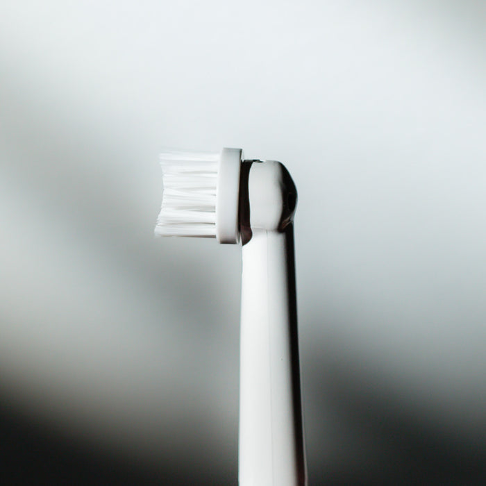 Close-up of the Plus Ultra eco-friendly Toothbrush Head Replacement - Oral-B, displaying its white bristles and sleek handle against a soft-focus gray background for seamless integration.