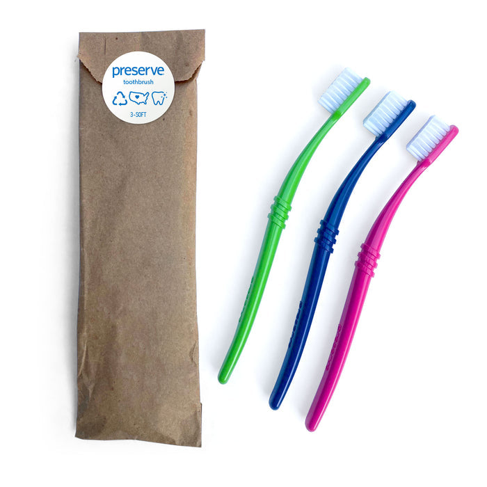 Three colorful toothbrushes—green, blue, and pink—are neatly arranged beside a brown package labeled Preserve Toothbrush (Soft). These brushes, made from recycled plastic, have white bristles and slightly curved handles for an eco-friendly clean.