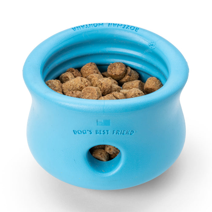 A small blue rubber treat dispensing toy from West Paw, containing brown kibble pieces. It has a rounded shape with a side hole and the text Dogs Best Friend, similar to West Paw Zogoflex designs, promoting healthy and slow eating.