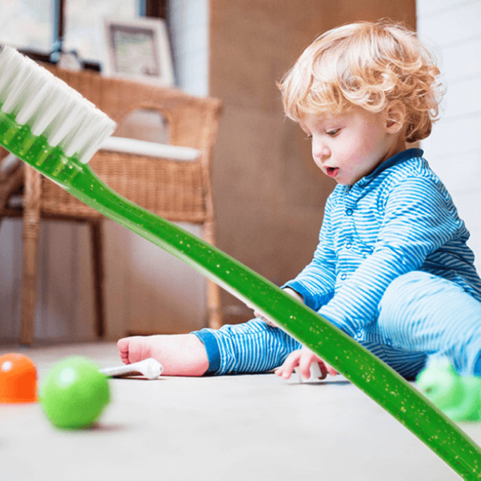 A young child in blue pajamas plays on the floor with toys, while a Radius Totz Toothbrush 18 mo+ is prominently placed in the foreground.