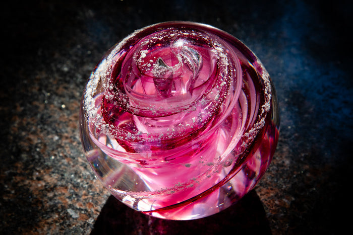 Pink tranquil swirl glass paperweight infused with cremation ash featuring curved ribbons and speckled accents