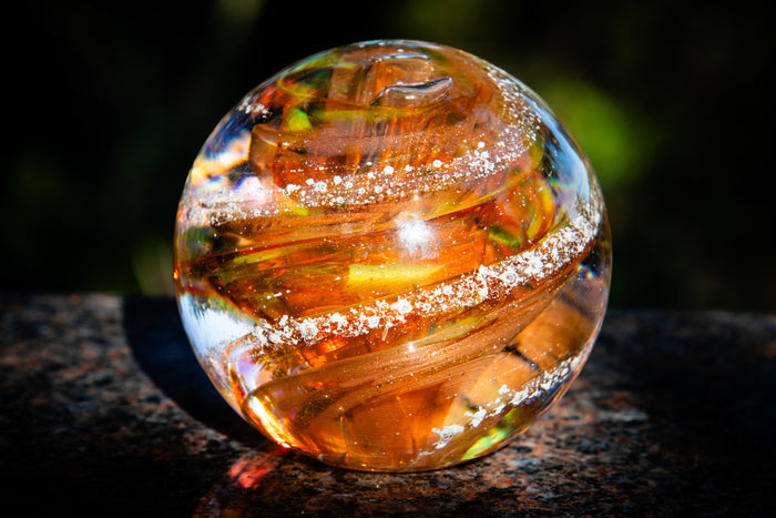Clear glass cremation orb with internal patterns on a dark surface