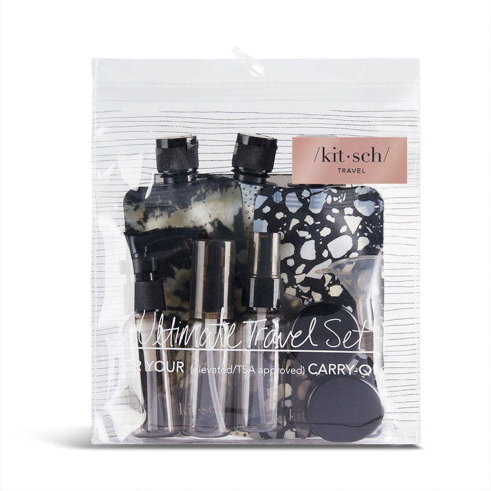 A clear, zippered pouch labeled Kitsch holds the Travel Bottle Set with eco-friendly, travel-size containers: BPA-free spray bottles, a black and white patterned case, and other small bottles designed for TSA-approved carry-on use.