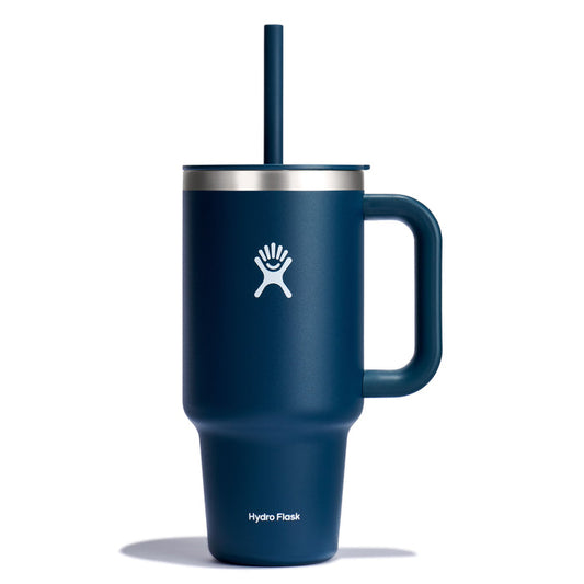 The 32 oz Hydro Flask Travel Tumbler is blue with a handle and straw, featuring a white logo. It has a sleek design, wide base, narrow middle, stainless steel rim, and double-wall vacuum insulation for excellent temperature retention.