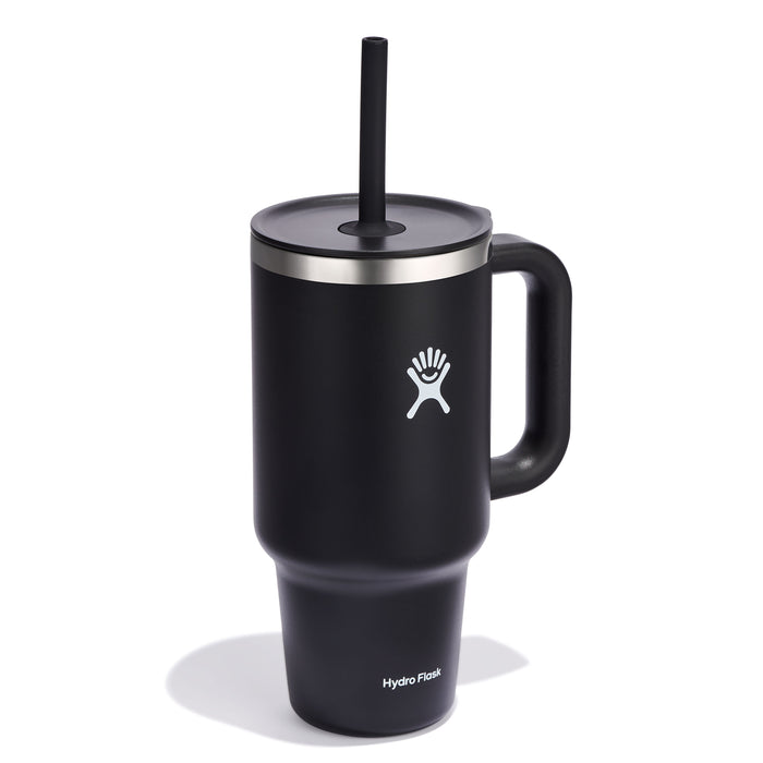 The 32 oz Travel Tumbler by Hydro Flask is a sleek black insulated tumbler with a handle, stainless steel rim, black straw, and double-wall vacuum insulation. It has a leak-resistant lid, features a stylized person with outstretched arms logo on the front, and the Hydro Flask name printed at the bottom.