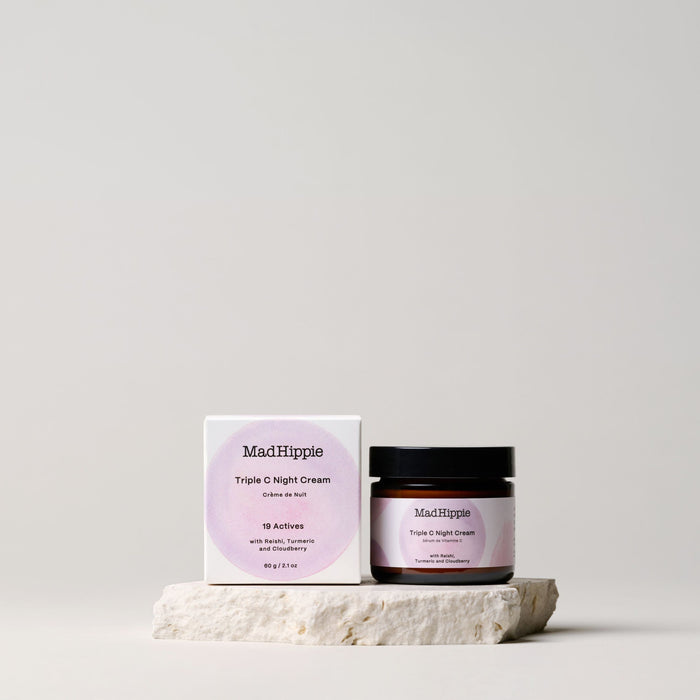 A jar and box of Mad Hippie Triple C Night Cream, enriched with vitamin C for natural skin care, sit on a small stone slab against a neutral backdrop. The open jar is next to the box, both showcasing minimalist packaging design.