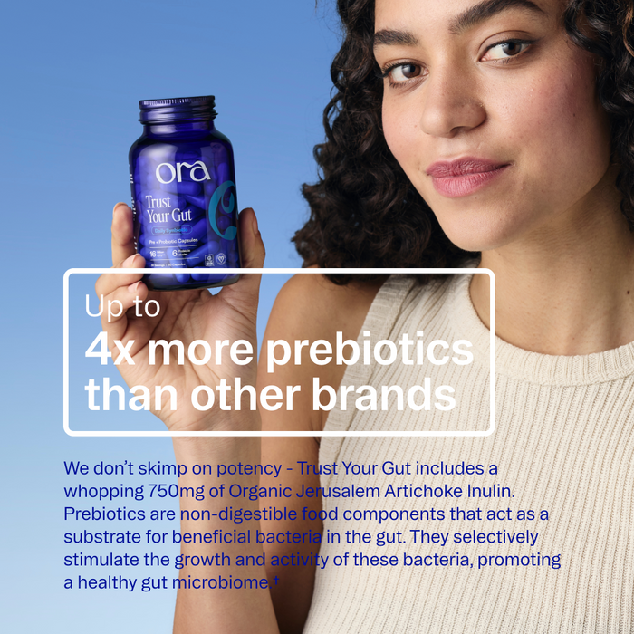 A woman in a white top holds a blue Ora Organic Trust Your Gut: Daily Pre + Probiotic Capsule jar, a synbiotic supplement with up to 4x more prebiotics than other brands and organic Jerusalem artichoke inulin for gut health.