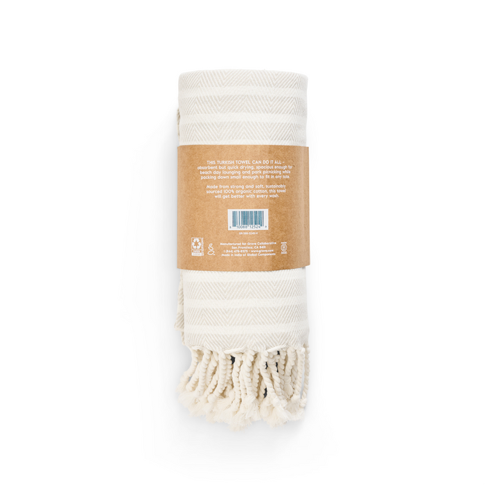 Grove Co.s Large Turkish Towel from the Spring Collection showcases a cream color, subtle zigzag pattern, and fringed edges. Made from organic cotton and wrapped in a brown label with text and barcode, its soft and eco-friendly.