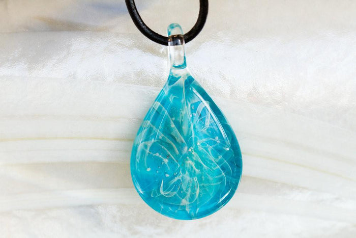 Turquoise teardrop glass pendant infused with cremation ashes hanging on a black cord