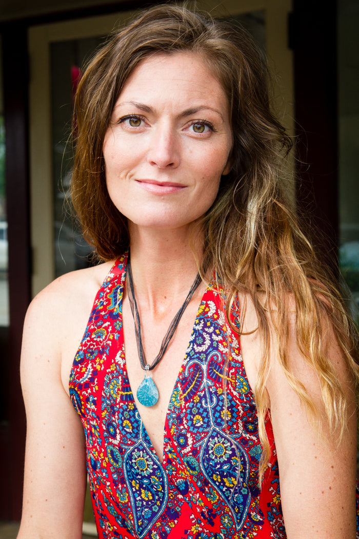Portrait of a woman wearing a turquoise ash infused glass pendant on a cord necklace outdoors.