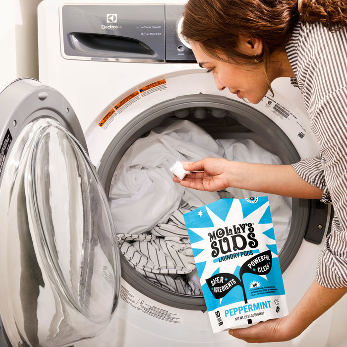 A woman places Molly's Suds Ultra Concentrated Laundry Detergent Pods into a front-loading washing machine filled with clothes.